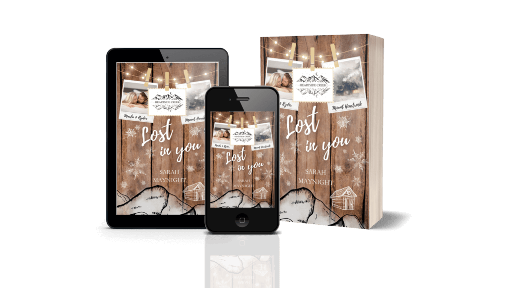 Mock up mit Tablet, Smartphone und Printbuch nebeneinander jeweils mit dem Cover von Heartside Creek: Lost in you. Jeweils abgebildet ist: Buchcover Roman Heartside Creek – Lost in you (Cosy New Adult Winter Romance): Hintergrund in Holzoptik mit angedeutetem stilisiertem Gebirge und der Silhouette einer Hütte im unteren Randbereich. An einer Lichterkette im oberen Bildbereich hängen drei Postkartenfotos. Auf dem ersten ein Paar, die unter einer Bettdecke hervorspitzen, eine blonde junge Frau und ein dunkelblonder junger Mann mit Bartansatz. In der Mitte ein Bild von einem stilisierten Gebirge mit der Bezeichnung Heartside Creek, dem Haupttitel der Buchreihe, und rechts ein Bild einer Nebelumwobenen Berghütte im Schnee. Die Bilder sind mit Holzwäscheklammern aufgehängt.