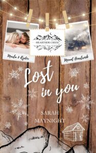 Buchcover Roman Heartside Creek – Lost in you (Cosy New Adult Winter Romance): Hintergrund in Holzoptik mit angedeutetem stilisiertem Gebirge und der Silhouette einer Hütte im unteren Randbereich. An einer Lichterkette im oberen Bildbereich hängen drei Postkartenfotos. Auf dem ersten ein Paar, die unter einer Bettdecke hervorspitzen, eine blonde junge Frau und ein dunkelblonder junger Mann mit Bartansatz. In der Mitte ein Bild von einem stilisierten Gebirge mit der Bezeichnung Heartside Creek, dem Haupttitel der Buchreihe, und rechts ein Bild einer Nebelumwobenen Berghütte im Schnee. Die Bilder sind mit Holzwäscheklammern aufgehängt.